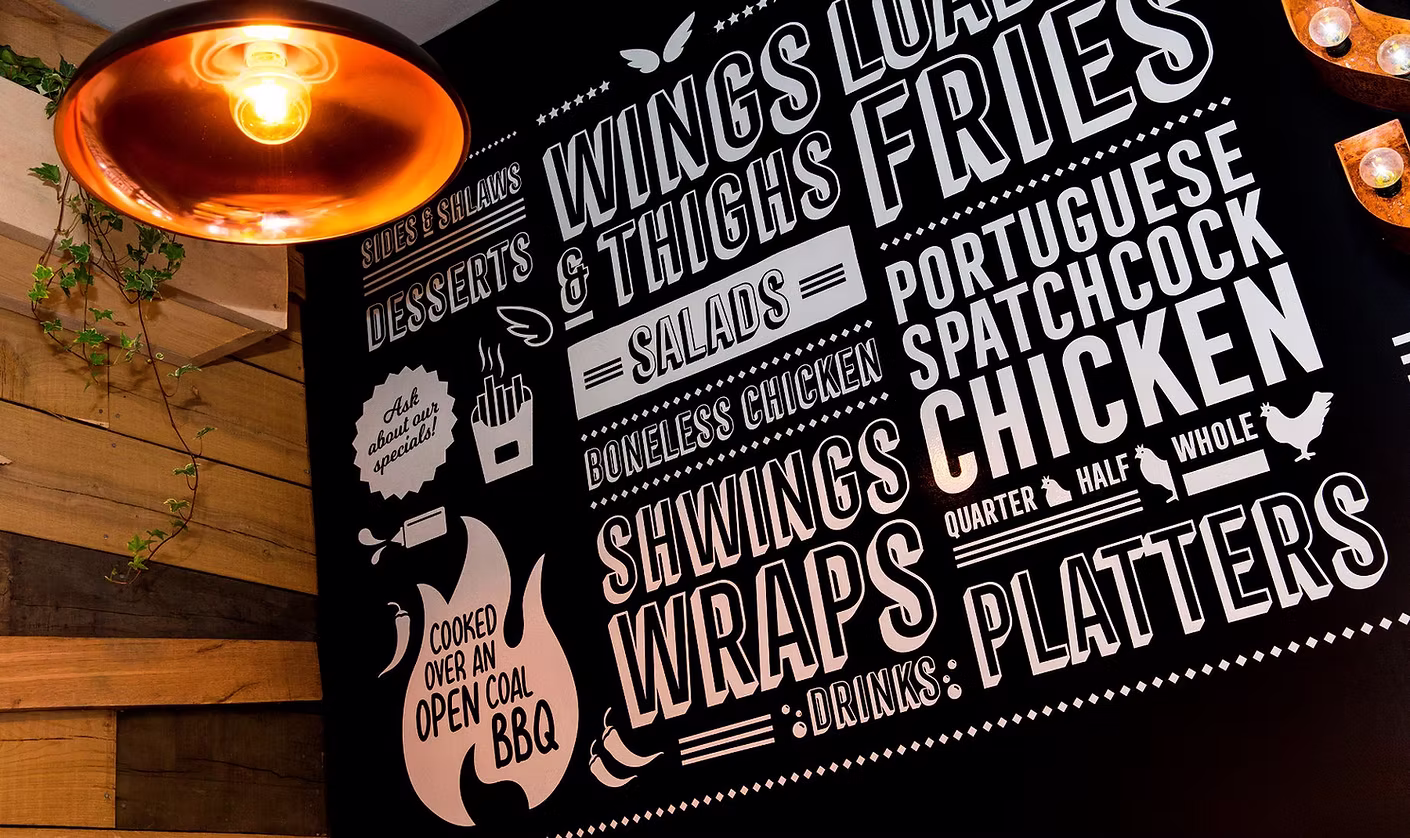 Shwings' black hand-painted menu wall listing wings, loaded fries, wraps, platters and 'cooked over an open coal BBQ'